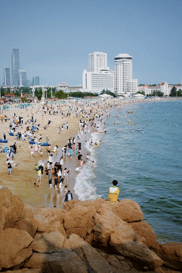 En lang strand på utsiden av en by, fullt av folk. Det ser ut som et tropisk område.